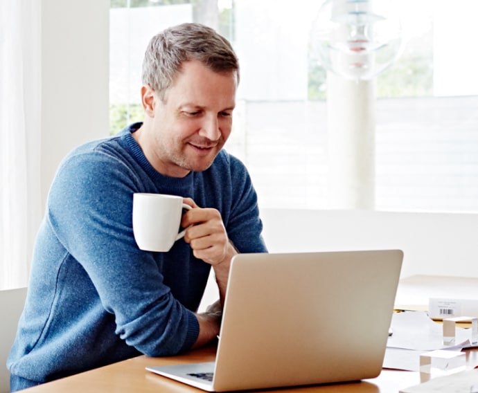 Hombre en su casa usando una computadora portátil y bebiendo café.