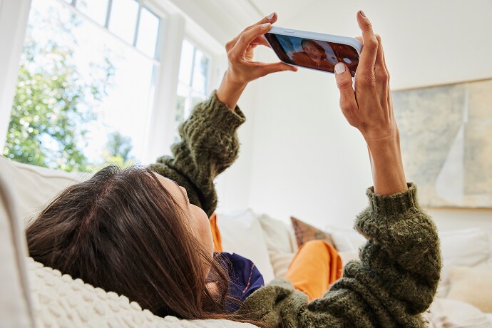 Mujer recostada mirando un teléfono celular
